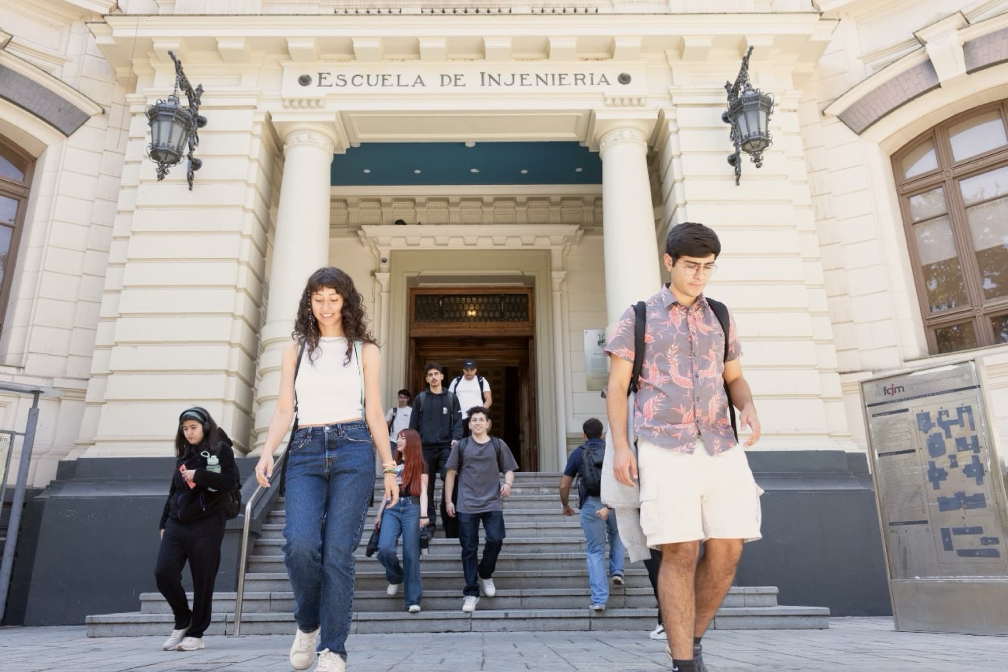 Students walk down the steps of the Escuela de Injeniería at Beauchef on a sunny day.