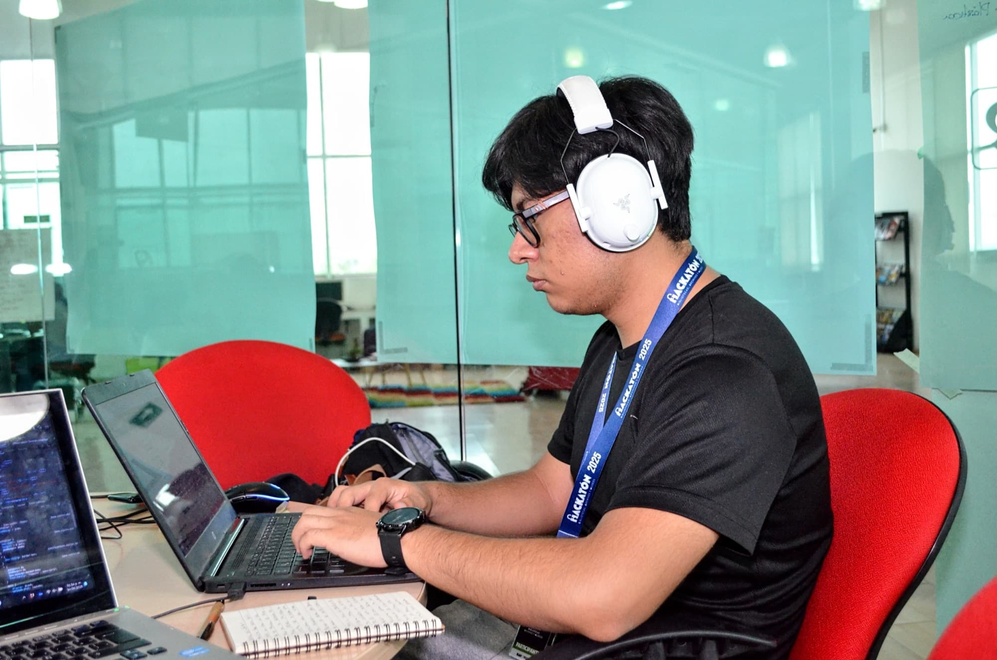 A student with headphones works late on a laptop, with a notebook beside it.