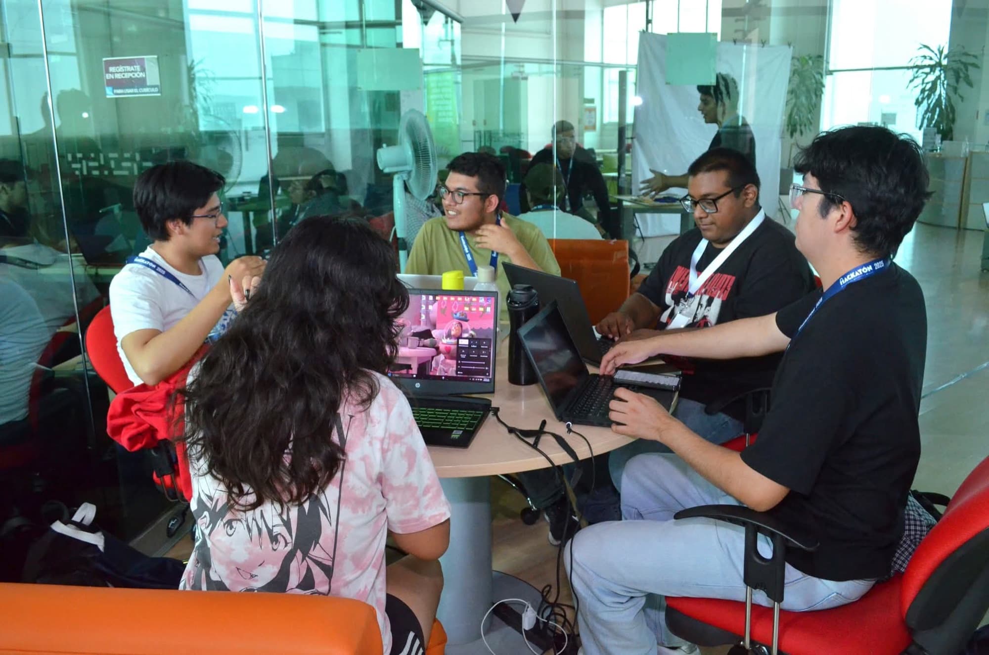 A team of four students works with laptops and notes at a round table.